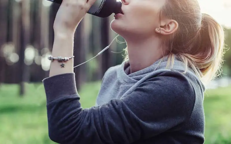 Young sporty woman drinking meal replacement shake from plastic cup in the park