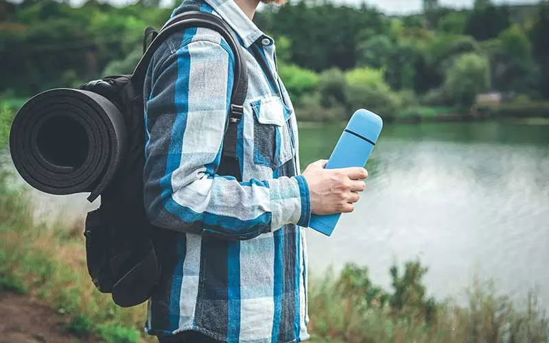  Young man with backpack holding yoga mat and flask