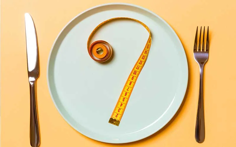 Measuring tape on a blue plate with fork and knife on a yellow background