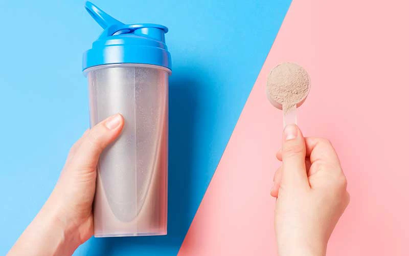 Female hand holds shaker with protein shake and scoop of Meal replacement shake powder