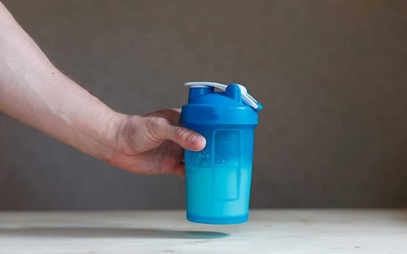 Hand holding plastic shaker with keto shake and glass on table
