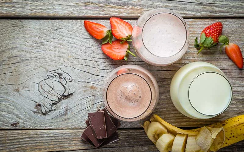Meal replacement shakes with strawberries, banana and chocolate on a wooden background