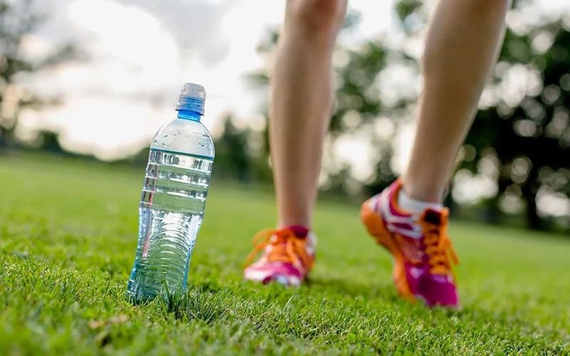 Runner athlete running with bottle of water on grass