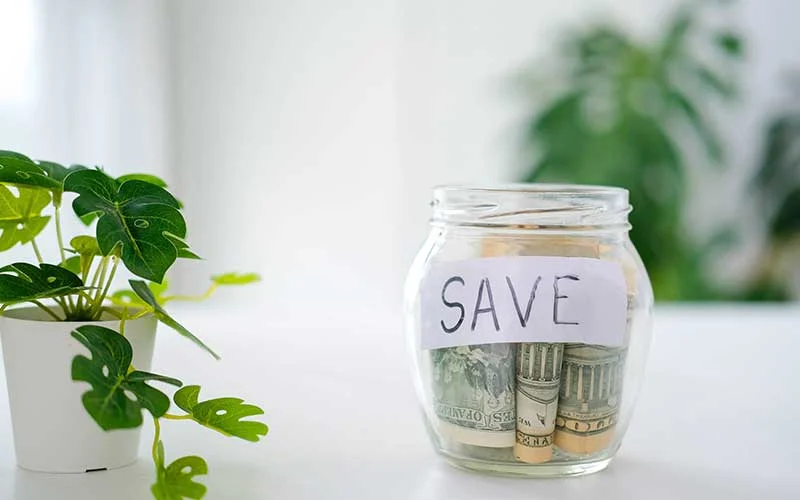 Glass jar with money and word save on white background