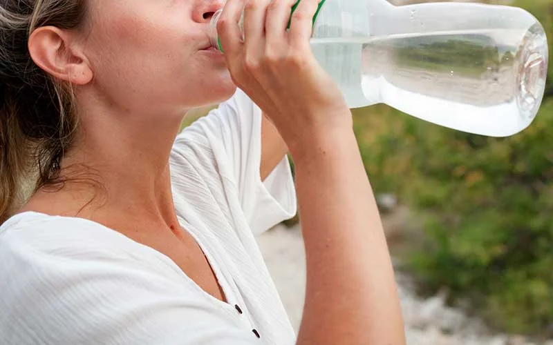 Tired woman on trekking trail drinking water.