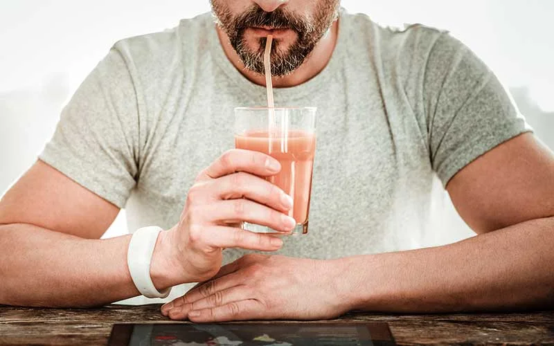A man drinking smoothie while reading news on the tablet