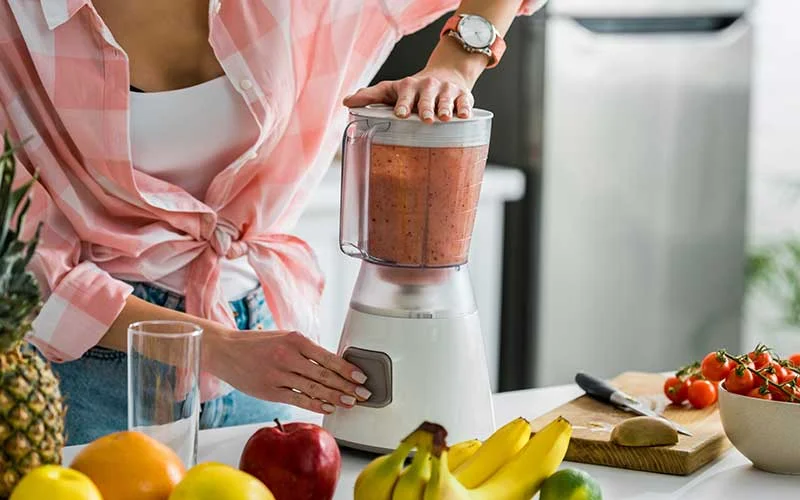 woman using blender in kitchen with healthy fruits