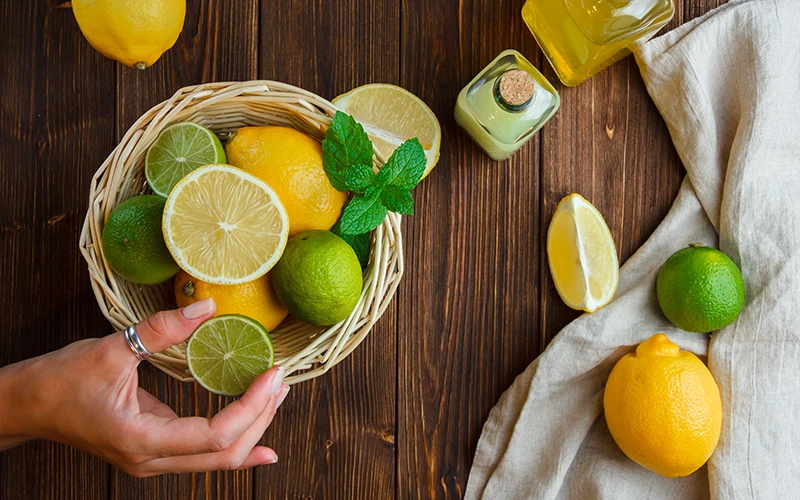  Lemons in a basket with white cloth hand holding half of lemon top view on a wooden surface