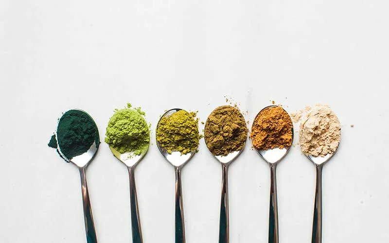 Spoons with different kinds of superfood powder on a white background
