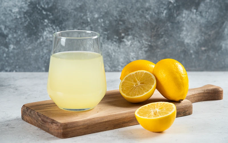 A glass cup of fresh lemon juice on a wooden board