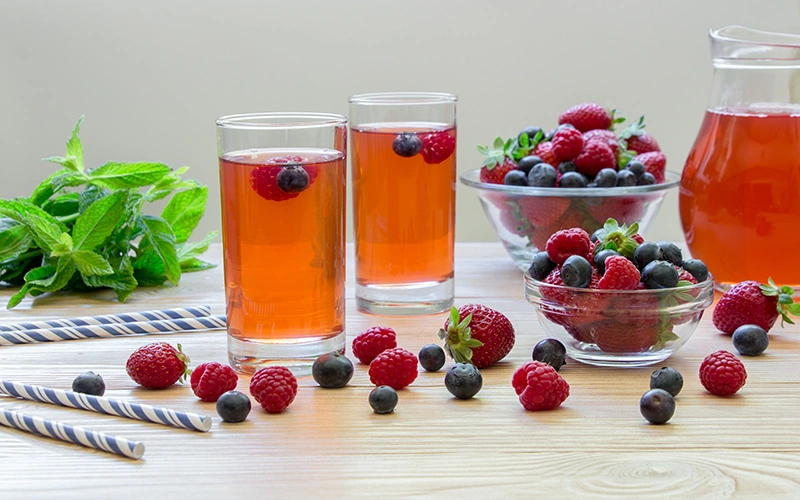 Two glasses of fruit juice with raspberries, blueberries and mint on a wooden table