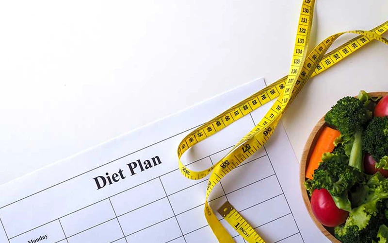 Diet plan with fresh vegetables and measuring tape on a white background.