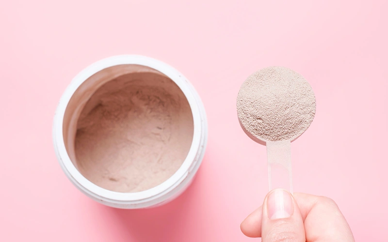 Chocolate meal replacement shake powder in scoop and plastic jar on pink background
