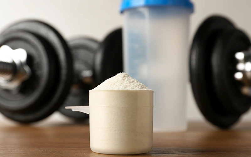 View of scoop with protein shake powder, shaker and dumbbells on table